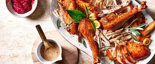 Image of a carved turkey covered with herbs with cranberry sauces on the side