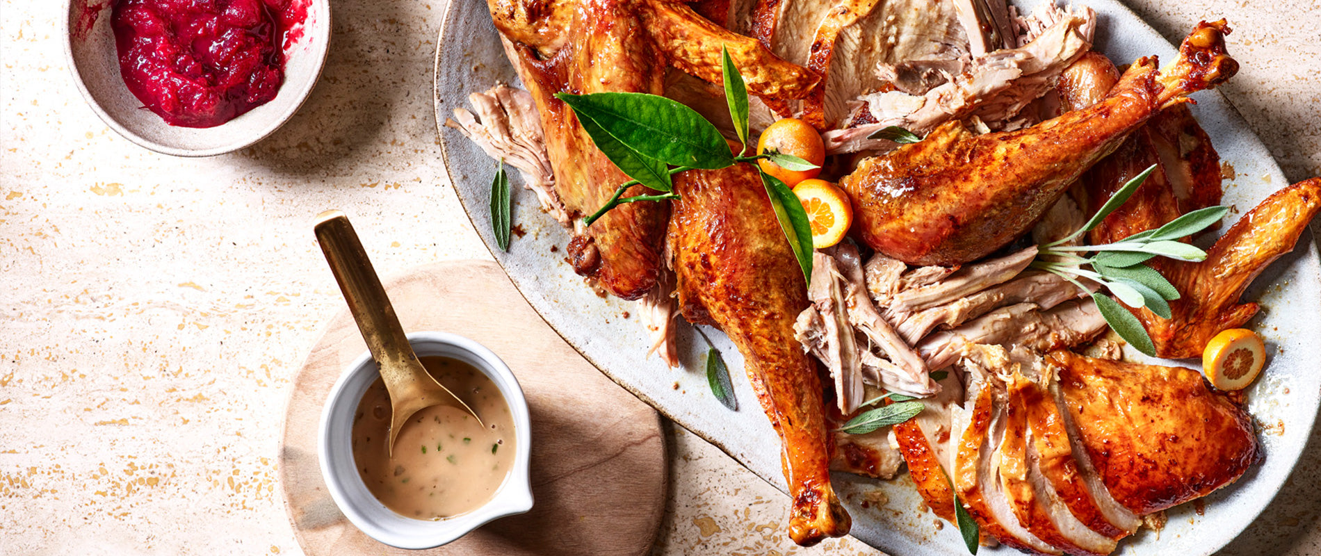 Image of a carved turkey covered with herbs with cranberry sauces on the side